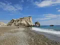 Skała Afrodyty na Cyprze, z turkusowym morzem i kamienistą plażą. Ludzie odpoczywają i spacerują.