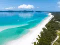 Rajskie australia plaże z turkusową wodą i białym piaskiem, na tle zielonych wzgórz. Wiele jachtów kołysze się na falach.