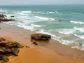 Maroko plaże: dwójka surferów wchodzi do wody z deskami, fale rozbijają się o skaliste wybrzeże.
