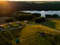 Idealne miejsce, gdzie pojechać na weekend: urokliwe domki nad jeziorem, otoczone zielenią i polami, w złotym świetle zachodzącego słońca.