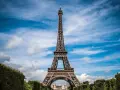 Majestatyczna wieża Eiffel w Paryżu, górująca nad zielonymi krzewami i błękitnym niebem z chmurami.