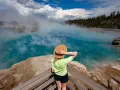 Kobieta w kapeluszu podziwia turkusowe gorące źródło w Yellowstone. Gdzie jest Yellowstone? Tu, wśród parujących wód i lasów.