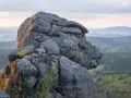 Skaliste formacje na tle zielonych gór w Czechach. Słońce oświetla skały, tworząc ciekawe cienie.