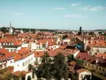 Widok na dachy Pragi, idealne miejsce na tani city break. W oddali wieże i kopuły.