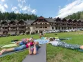 Dzieci i dorośli leżą na matach na trawie przed hotelem, ciesząc się relaksującym weekendem w górach.