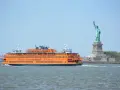 Pomarańczowy prom Staten Island Ferry płynie obok Statuy Wolności.