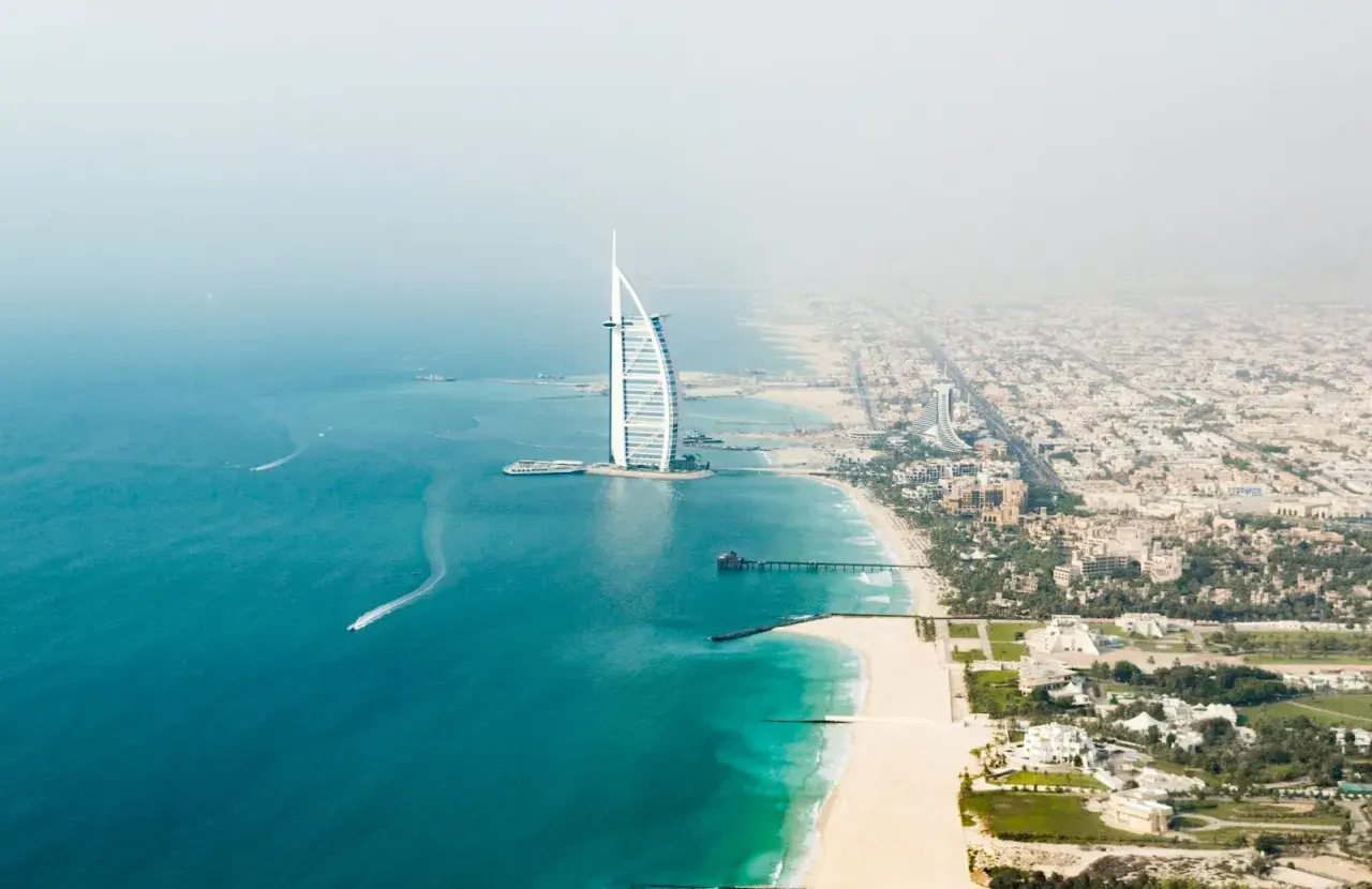 Widok z lotu ptaka na Dubaj: luksusowy hotel w kształcie żagla, piaszczysta plaża i turkusowe morze.