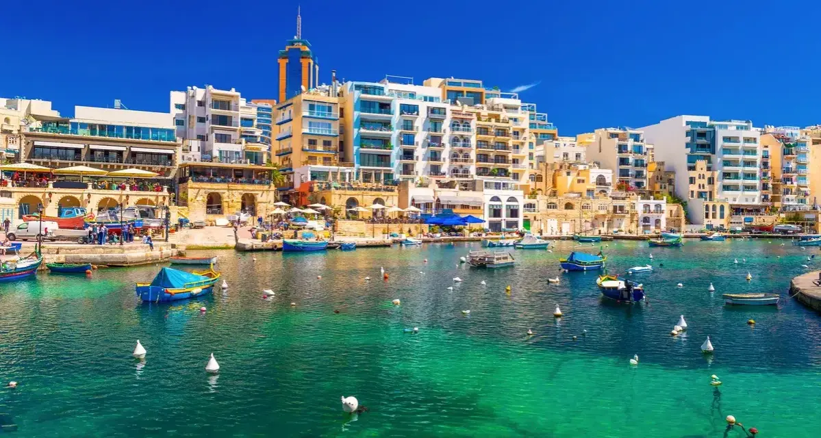 Malta, gdzie na Malcie jest tak pięknie! Woda krystalicznie czysta, łodzie kołyszą się na falach, a w tle kolorowe budynki.