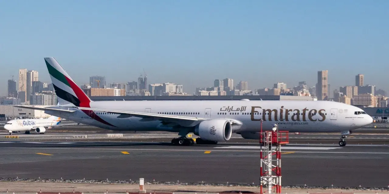 Samolot Emirates na płycie lotniska, w tle panorama Dubaju. Zastanawiasz się, ile się leci do Dubaju?