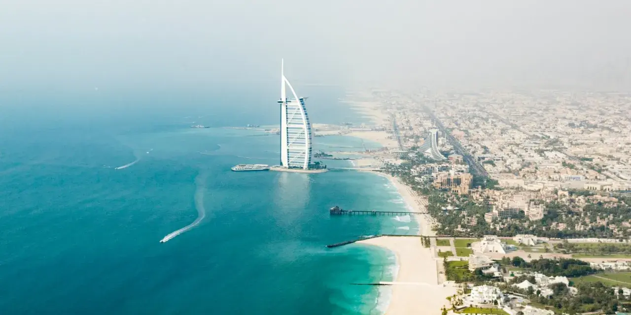 Widok z lotu ptaka na Dubaj: luksusowy hotel w kształcie żagla, piaszczysta plaża i turkusowe morze.