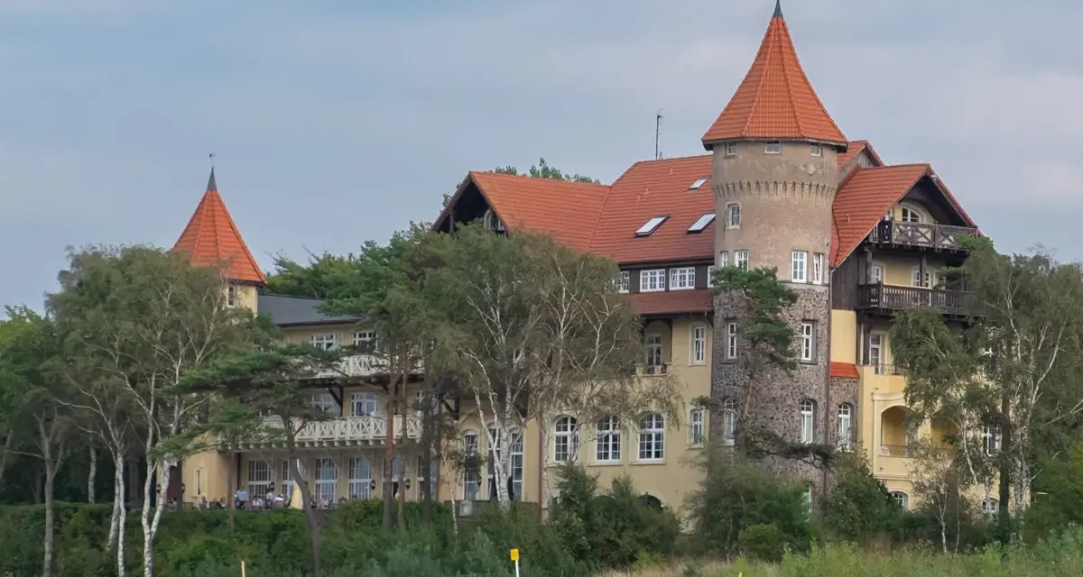 Elegancki hotel z wieżą i czerwonym dachem, otoczony drzewami, idealny na łeba atrakcje dla dorosłych.