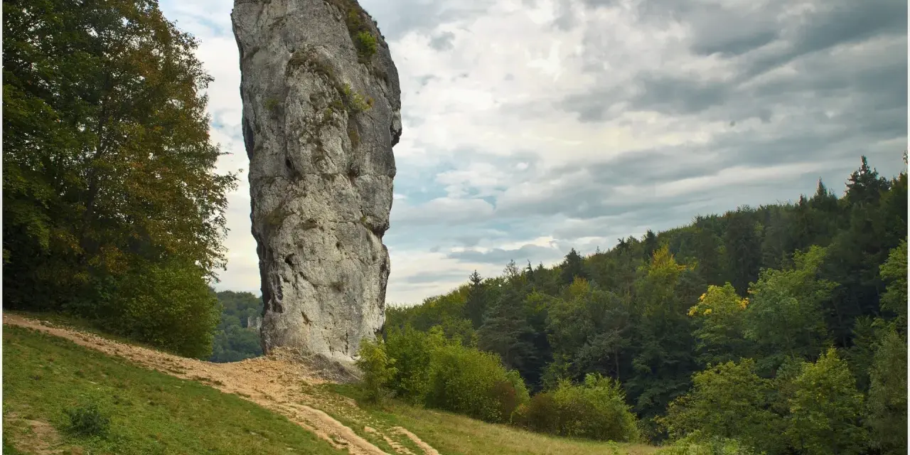 Maczuga Herkulesa, wysoka skała wapienna, stoi samotnie na tle zielonego lasu i burzowego nieba.