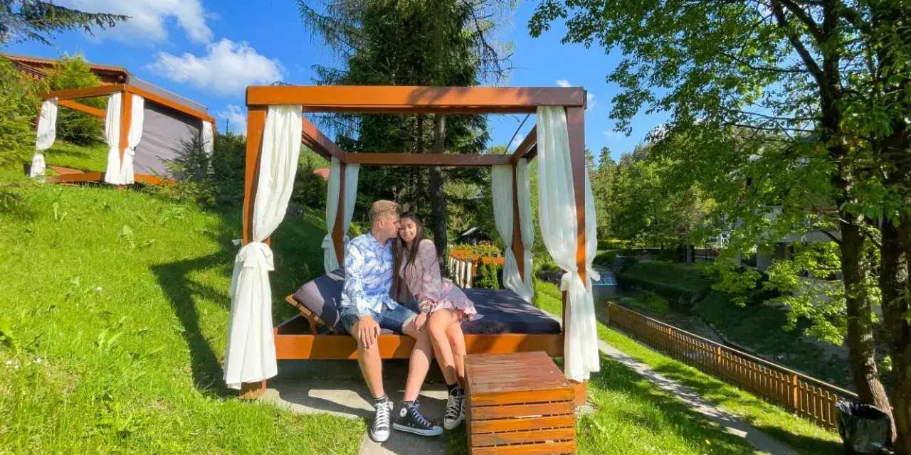 Idealne miejsce, gdzie na weekend we dwoje. Para odpoczywa na łóżku pod baldachimem w otoczeniu zieleni.