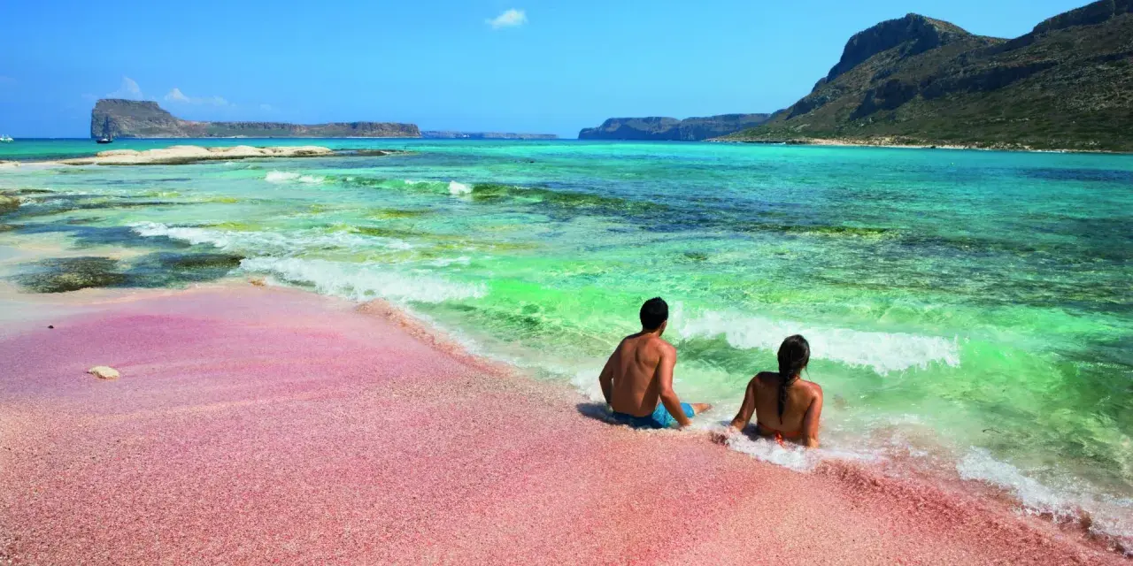 Para relaksuje się na różowej plaży Elafonisi na Krecie, z turkusową wodą i skalistymi wyspami w tle.