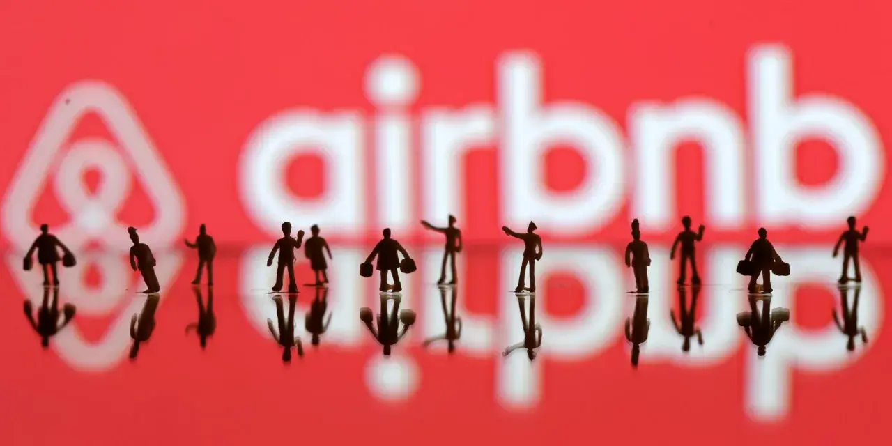 Małe figurki ludzi na tle logo Airbnb. Zastanawiasz się airbnb co to? To platforma do rezerwacji noclegów.
