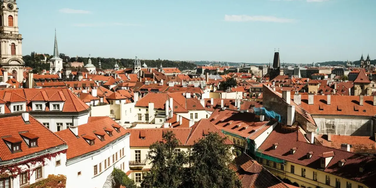 Widok na dachy Pragi, idealne miejsce na tani city break. W oddali wieże i kopuły.