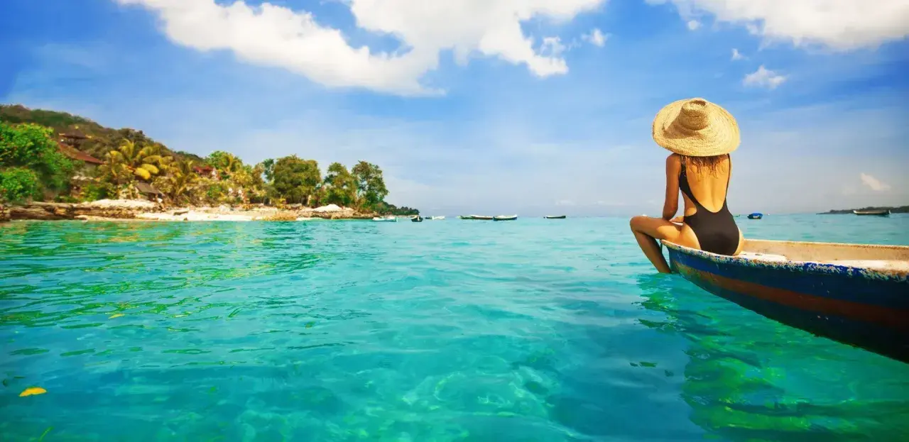 Kobieta w kapeluszu siedzi na łodzi, podziwiając turkusowe morze i tropikalne plaże na Bali.