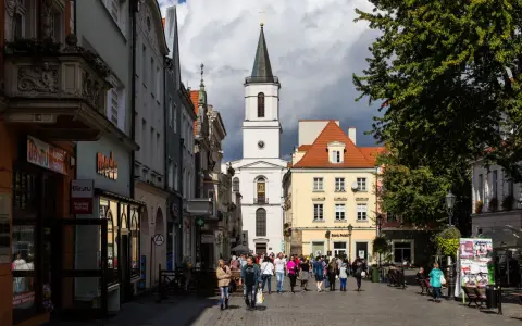 Ulica w jednym z miast na zachodzie Polski, z kościołem w tle i ludźmi spacerującymi po rynku.