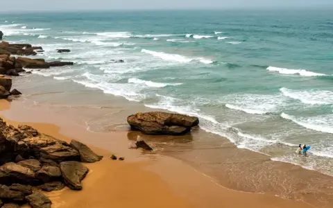 Maroko plaże: dwójka surferów wchodzi do wody z deskami, fale rozbijają się o skaliste wybrzeże.