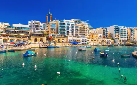 Malta, gdzie na Malcie jest tak pięknie! Woda krystalicznie czysta, łodzie kołyszą się na falach, a w tle kolorowe budynki.