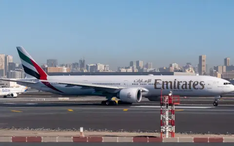 Samolot Emirates na płycie lotniska, w tle panorama Dubaju. Zastanawiasz się, ile się leci do Dubaju?