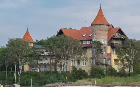 Elegancki hotel z wieżą i czerwonym dachem, otoczony drzewami, idealny na łeba atrakcje dla dorosłych.