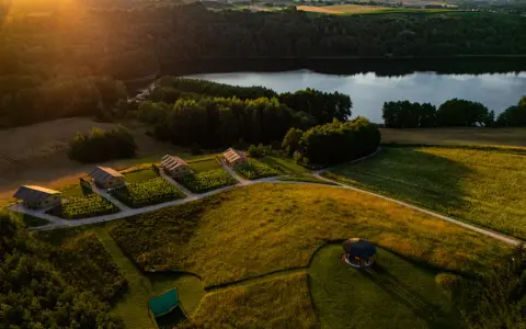 Idealne miejsce, gdzie pojechać na weekend: urokliwe domki nad jeziorem, otoczone zielenią i polami, w złotym świetle zachodzącego słońca.