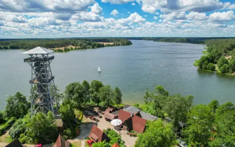 Wieża widokowa nad jeziorem, idealne miejsce, by poczuć magię Kaszub. Żaglówka na wodzie, lasy i błękitne niebo.