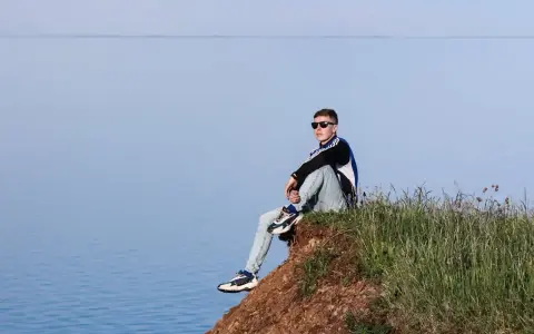 Chłopak siedzi na skarpie nad jeziorem, zastanawiając się, gdzie na wakacje z nastolatkiem w Polsce.