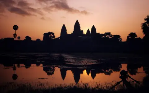 Zachód słońca nad Angkor Wat, idealne tło dla niezapomnianych kambodżańskich wakacji. Widok odbija się w wodzie, a na pierwszym planie statyw z aparatem.