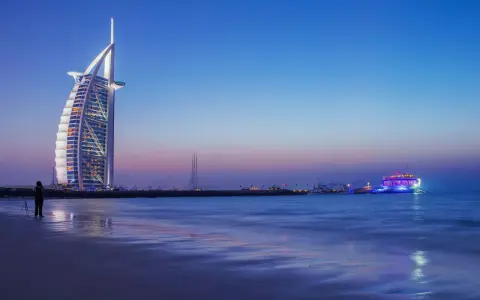 Zachód słońca nad Zatoką Perską. Widok na hotel Burj Al Arab i oświetloną łódź. Ceny w Dubaju mogą być wysokie, ale widoki są bezcenne.
