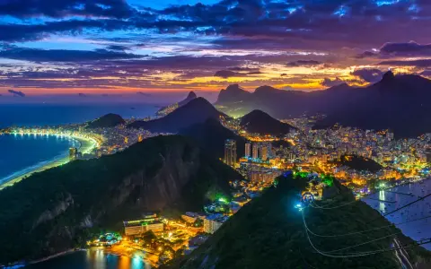 Zachód słońca nad słynną plażą w Rio de Janeiro. Miasto rozświetlone tysiącami świateł, góry i ocean tworzą magiczny widok.