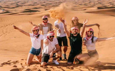 Grupa przyjaciół w tradycyjnych arabskich chustach bawi się piaskiem na pustyni. Wspaniałe wspomnienia z Dubaju w styczniu.