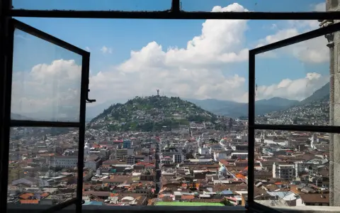 Widok na miasto z otwartego okna, z wzgórzem i pomnikiem w tle. To piękna panorama stolicy Ekwadoru, ze stolicą w Quito.