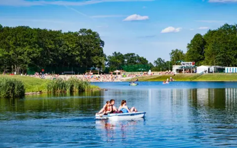 Rodzina na rowerku wodnym na jeziorze, plaża pełna ludzi, las i budynki w tle. Idealne miejsce gdzie nad wodę Dolny Śląsk.