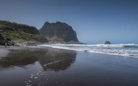 Dziecko bawi się na czarnej plaży Madera, w tle widać skaliste klify i ocean.
