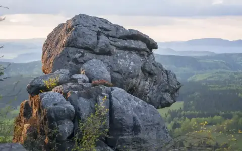 Skaliste formacje na tle zielonych gór w Czechach. Słońce oświetla skały, tworząc ciekawe cienie.