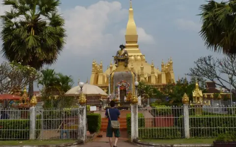 Złota stupa Pha That Luang, symbol stolicy w Wientianie, otoczona palmami i zielenią.