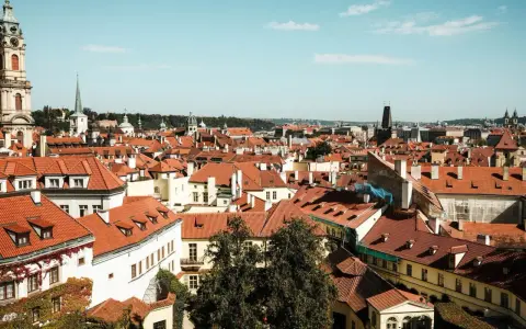 Widok na dachy Pragi, idealne miejsce na tani city break. W oddali wieże i kopuły.