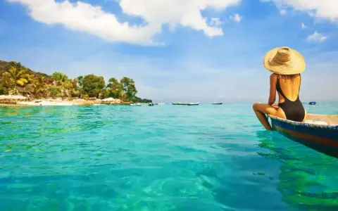Kobieta w kapeluszu siedzi na łodzi, podziwiając turkusowe morze i tropikalne plaże na Bali.
