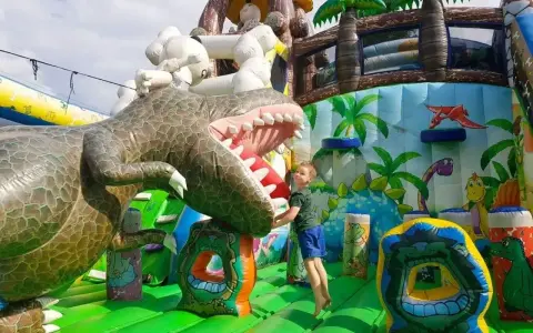 Chłopiec skacze na dmuchanym dinozaurze. Wspaniała atrakcja dla dzieci, jedno z wielu **ciekawe miejsca do 100 km od Katowic**.