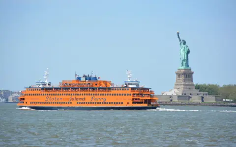 Pomarańczowy prom Staten Island Ferry płynie obok Statuy Wolności.
