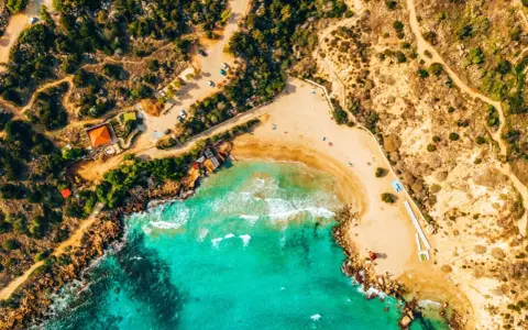 Widok z lotu ptaka na piaszczystą plażę z turkusową wodą. Idealne miejsce, by pomyśleć, co zabrać na Cypr: strój kąpielowy, krem z filtrem i dobry humor!