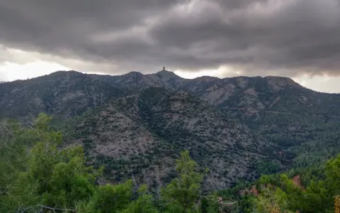 Góry Troodos pod burzliwym niebem. W oddali na szczycie widać charakterystyczną budowlę.