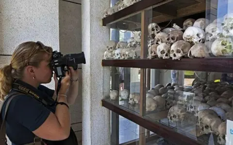 Kobieta fotografuje ludzkie czaszki na wystawie upamiętniającej pola śmierci w Kambodży.