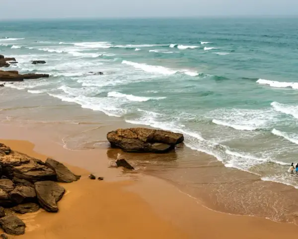 Maroko plaże: dwójka surferów wchodzi do wody z deskami, fale rozbijają się o skaliste wybrzeże.