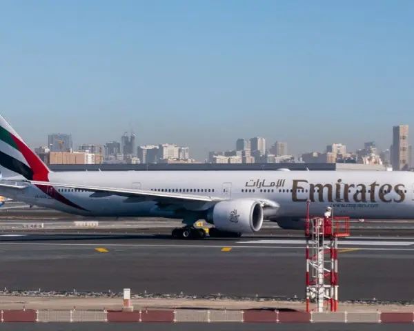 Samolot Emirates na płycie lotniska, w tle panorama Dubaju. Zastanawiasz się, ile się leci do Dubaju?