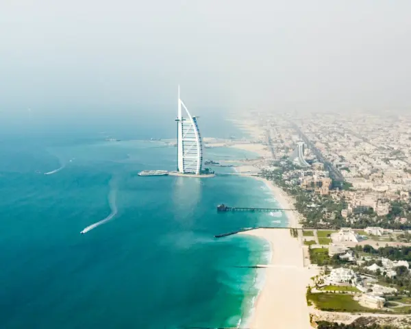 Widok z lotu ptaka na Dubaj: luksusowy hotel w kształcie żagla, piaszczysta plaża i turkusowe morze.