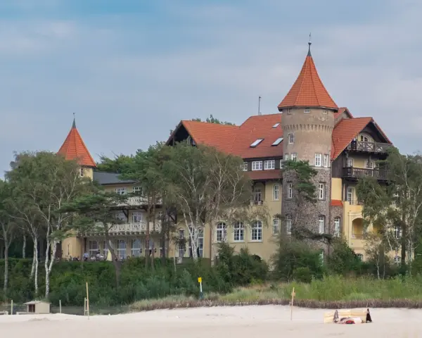 Elegancki hotel z wieżą i czerwonym dachem, otoczony drzewami, idealny na łeba atrakcje dla dorosłych.
