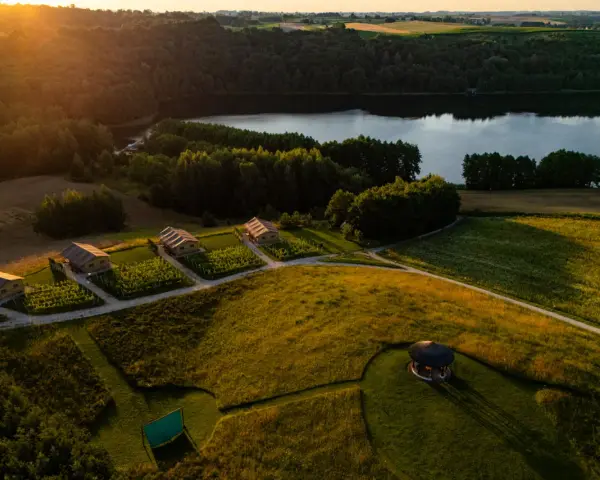 Idealne miejsce, gdzie pojechać na weekend: urokliwe domki nad jeziorem, otoczone zielenią i polami, w złotym świetle zachodzącego słońca.